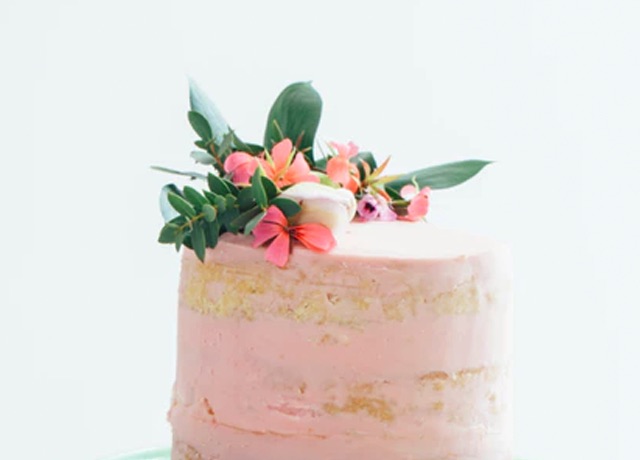 Side-view of cake frosted with pink icing and garnished with flowers on top.